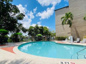 una piscina con sillas y sombrillas junto a un edificio en The Palms Inn & Suites Miami, Kendall, FL, en Kendall