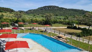 a swimming pool with red umbrellas and a mountain at Safaritent Glamping de L'Olivigne in Bize-Minervois