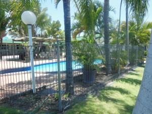 a fence around a swimming pool with palm trees at Country Road Motel in Charters Towers