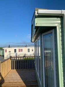 a green building with a glass door on a deck at Immaculate 2-Bed Lodge in Monreith in Newton Stewart