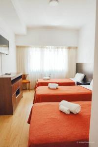 Habitación de hotel con 3 camas con sábanas de color naranja en Argentino Hotel en Mar del Plata