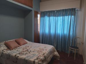 een slaapkamer met een bed en een raam met blauwe gordijnen bij Feliz Estadia in Mendoza