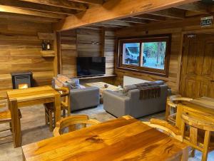 ein Wohnzimmer mit Holzwänden und Tischen sowie einem TV in der Unterkunft Illi Lodge & Hostel in Ranco