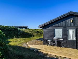 eine schwarze Hütte mit einer Holzterrasse mit einem Tisch und Stühlen in der Unterkunft 5 person holiday home in Fanø in Fanø