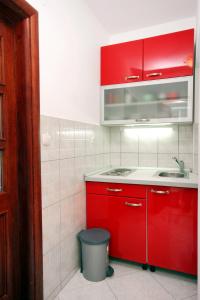 uma cozinha com armários vermelhos, um lavatório e uma lata de lixo em Family friendly apartments with a swimming pool Rogoznica - 7557 em Rogoznica