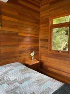 a bedroom with wooden walls and a bed and a window at CHALÉ DOS ALPES VERDES in Canela