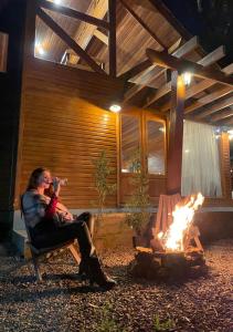 a woman sitting in a chair next to a fire at CHALÉ DOS ALPES VERDES in Canela