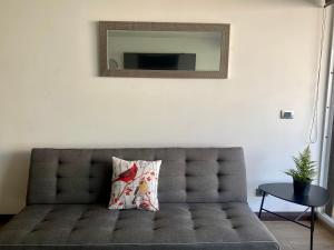 a gray couch with a pillow and a mirror on the wall at Departamento a pasos de Clinica Las Condes- Estoril in Santiago