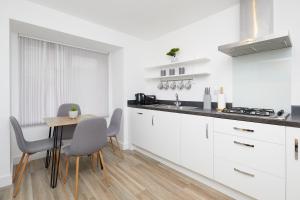 een keuken met witte kasten en een tafel en stoelen bij Royal Derby Hospital Mickleover Town House in Derby