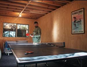 un uomo in piedi in una stanza con un tavolo da ping pong di Ponga eco-lodge a Hahei