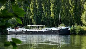 a boat floating on the water near a forest at Péniche Daphné's in Auvers-sur-Oise