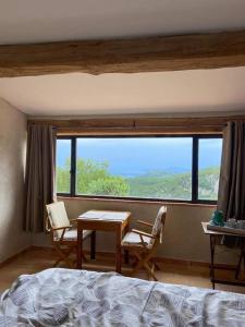 1 dormitorio con mesa, sillas y ventana grande en Le Cabanon de Gourdon bergerie rénové en pierre vue mer en Gourdon