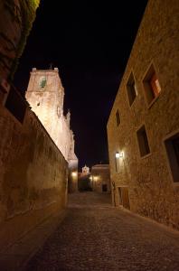 an empty alley with a clock tower at night at Atrio Restaurante Hotel 5 Estrellas - 3 Llaves Michelan in Cáceres