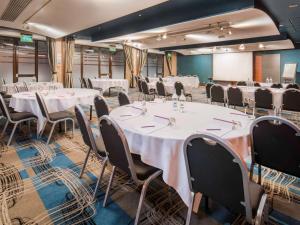 une salle de conférence avec des tables et des chaises blanches dans l'établissement Mercure London Heathrow Airport, à Hillingdon