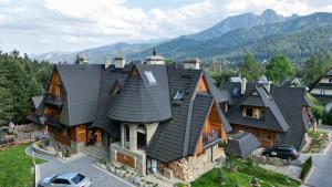 a house with a black roof with mountains in the background at Aparthotel Delta Royal in Kościelisko