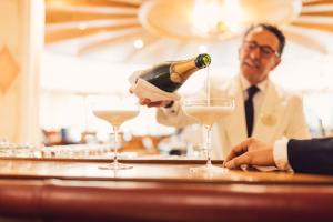 un homme versant une bouteille de champagne en deux verres dans l'établissement Alpenpalace Luxury Hideaway & Spa Retreat, à Lutago