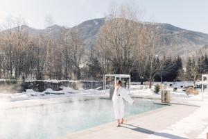 una donna in abito bianco in piedi accanto a una piscina d'acqua di Alpenpalace Luxury Hideaway & Spa Retreat a Lutago