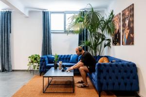 Ein Mann, der auf einer blauen Couch im Wohnzimmer sitzt in der Unterkunft PAME Wild in Athen