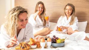 three women sitting in bed eating food and drinking juice at Sanadome Nijmegen in Nijmegen