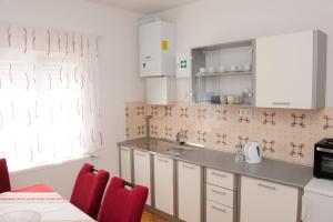 una cocina con armarios blancos, sillas rojas y fregadero en Apartman Noa 16, en Ðurđevac