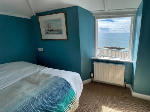 een blauwe slaapkamer met een bed en 2 ramen bij Bell Cliff House in Lyme Regis