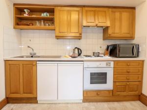 cocina con armarios de madera, fregadero y microondas en The Hayloft en Keswick