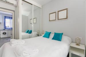 a white bedroom with a large white bed with blue pillows at FANTÁSTICO APARTAMENTO MADRID RIÓ-PUERTA DEL ÁNGEL in Madrid