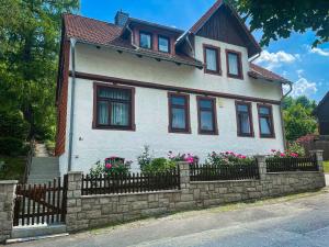 uma casa branca com uma cerca de pedra e flores rosas em Ferienwohnungen Marianne Lau em Wernigerode