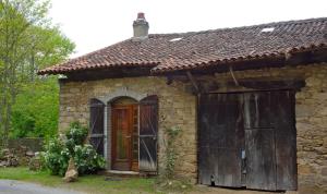 uma velha casa de pedra com uma porta e um portão em Couleurs du Daumail em Saint-Priest-sous-Aixe