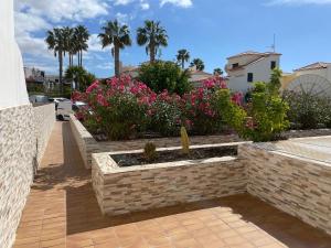 un jardín con flores rosas y una pared de ladrillo en The Palms 2 Bed Duplex with Pool View, en San Miguel de Abona