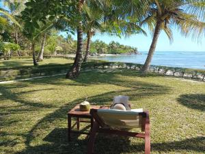 a table and a chair on the grass near the beach at La Tiaré île aux Nattes in Sainte Marie