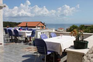 a patio with white tables and blue chairs and the ocean at Apartments and rooms by the sea Mali Losinj (Losinj) - 7977 in Mali Lošinj