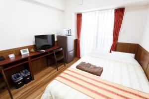 Hotel Peacely In Miyakojima Nexus في جزيرة مياكو: غرفة نوم بسرير ومكتب مع تلفزيون