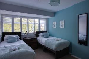 - 2 lits dans une chambre aux murs bleus et aux fenêtres dans l'établissement SAXON ROAD - A 3 Bedroom House with Garden by Prestigious Stays - Includes Wifi, Netflix & Amazon Alexa, à Sunbury Common