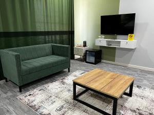 uma sala de estar com um sofá verde e uma televisão em KRich Hotel Aktobe em Aqtöbe