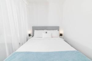 a white bedroom with a large white bed with blue sheets at White Innk city center apartment in Trnava