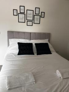 a white bed with black pillows and pictures on the wall at Modern Suite- Bedford City centre with free gym & parking in Bedford