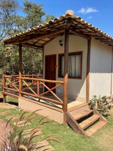 une petite maison avec une terrasse couverte en bois dans l'herbe dans l'établissement Pousada Villa Recanto dos Lagos, à Brumadinho