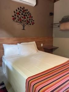 Un dormitorio con una cama blanca con una pintura floral en la pared en Pousada Villa Recanto dos Lagos, en Brumadinho