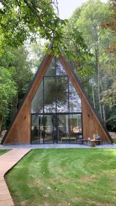uma casa de vidro com um telhado triangular num parque em La Maison Villeneuve - Lodges avec bains nordiques em Donnay