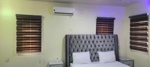 a bedroom with a bed with a gray headboard and windows at Premium 3 Bedroom Villa Upscale Alagbaka Area in Akure
