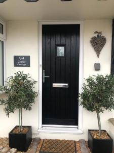 a black front door of a house with two potted trees at Corner Cottage - character, charm, great location. in Ringwood