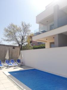 a swimming pool with blue chairs and a house at Villa apartment Laganini in Okrug Gornji