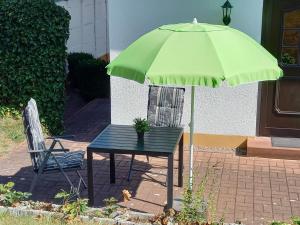 einen Tisch, einen grünen Regenschirm und zwei Stühle in der Unterkunft Ferienwohnung Schmalkalden am Radwanderweg in Schmalkalden