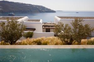 a building with a swimming pool in front of a body of water at Kalesma Mykonos in Ornos