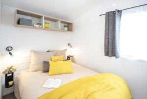 a bedroom with a bed with a yellow blanket on it at Camping Le Suroit in Le Bois-Plage-en-Ré
