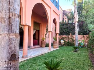 una casa rosa con césped delante en CYCAS VILLA TARGA GARDEN -Only Family, en Marrakech