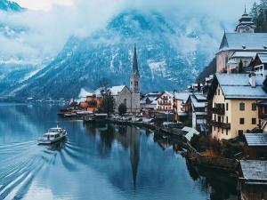 a town on the water with a church and a boat at Pension Cafe zum Mühlbach in Hallstatt