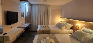 ナタールにあるFlat Maravilhoso na praia - Ilusion Hotelのベッド2台とテレビが備わるホテルルームです。
