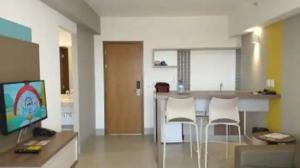 a living room with a kitchen with a bar with white chairs at Apartamento Resort em Olímpia in Olímpia